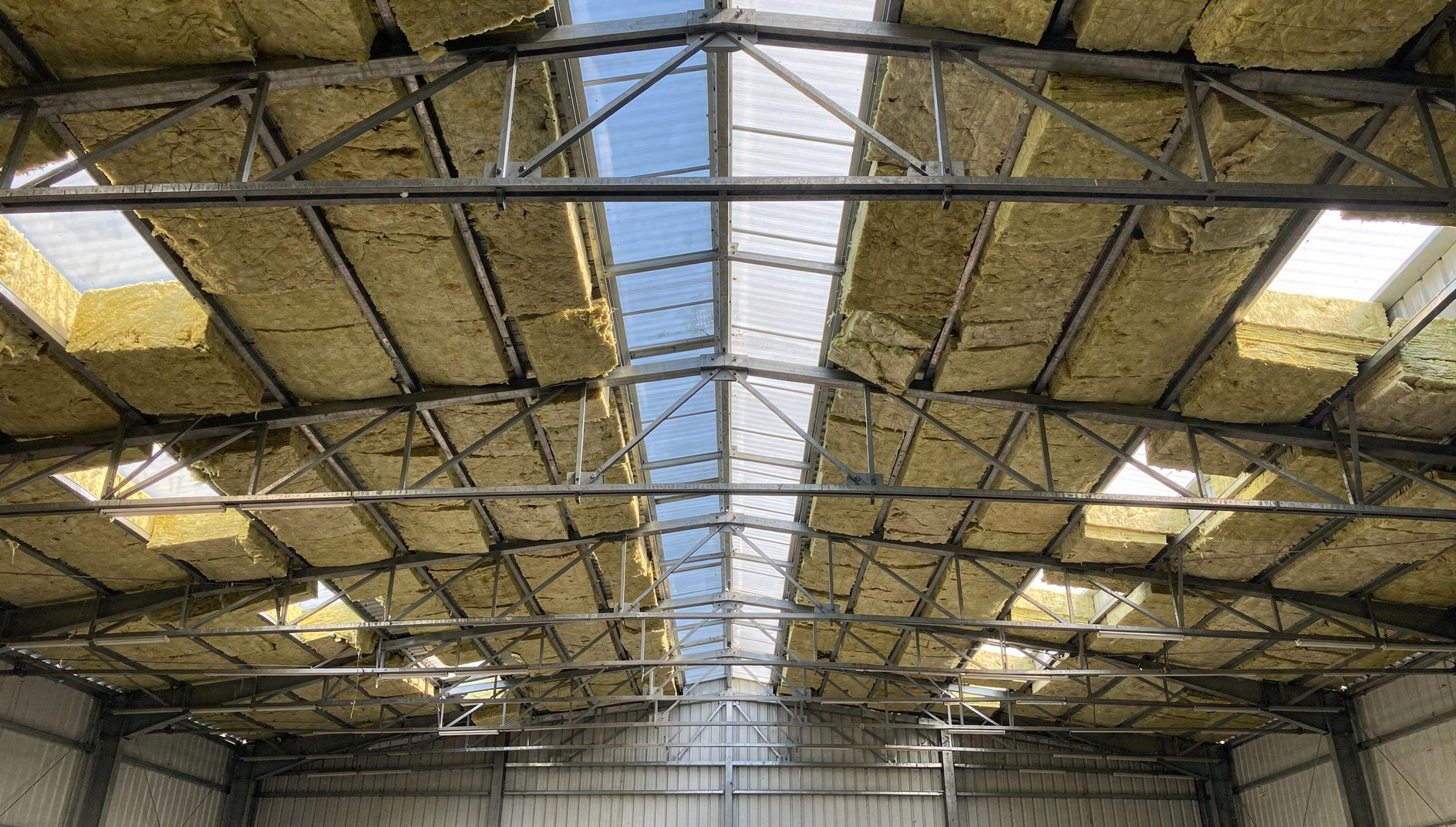 Charpente métallique d'un bâtiment industriel vue de l'intérieur avec des panneaux de laine minérale posés entre les pannes